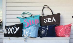 Vibrant collection of beach bags arranged on a white wooden table against a panel wall.